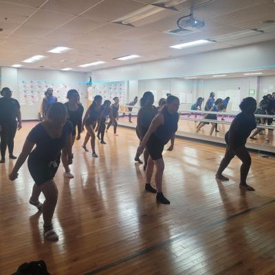 Silhouetted students lunge in unison, spread out in a rehearsal studio.