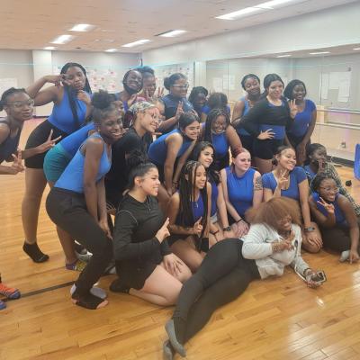 A group of young, racially diverse dance students  smiling and posing for a photo in black and blue dancewear.